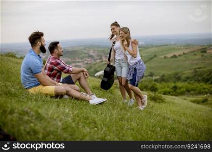 Group od young people sitting on grass and having fun on a field trip in nature on a mountain