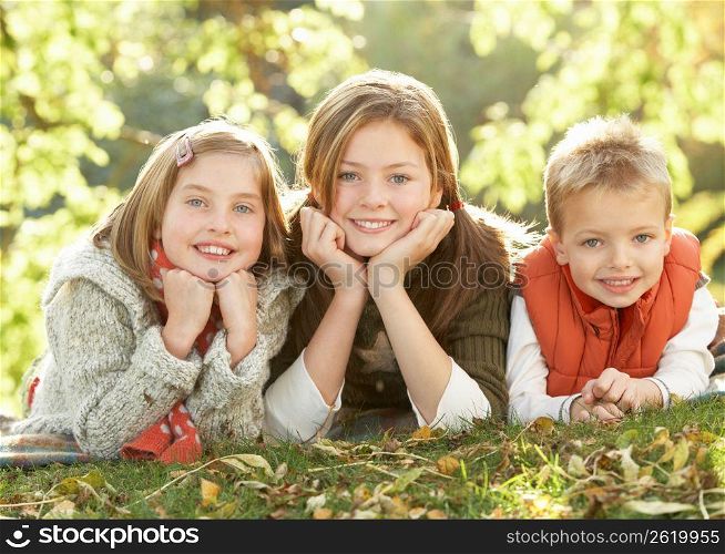 Group Of 3 Children Realxing Outdoors In Autumn Landscape