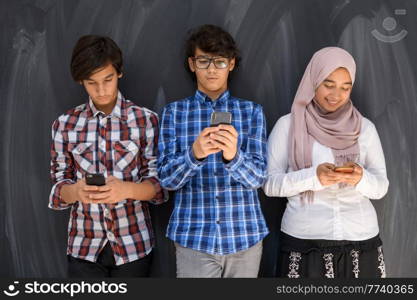 Group of Arab teens taking selfie photos on a smartphone with a black chalkboard in the background. Selective focus. High quality photo. Group of arab teens taking selfie photo on smart phone with black chalkboard in background. Selective focus