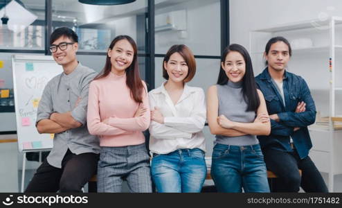 Group of Asia young creative people in smart casual wear smiling and arms crossed in creative office workplace. Diverse Asian male and female stand together at startup. Coworker teamwork concept.
