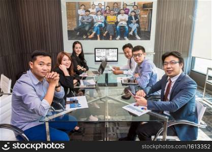 Group of asian Business team having video conference with another colleague team with their manager via technology monitor display in the modern conference room, Business people meeting concept