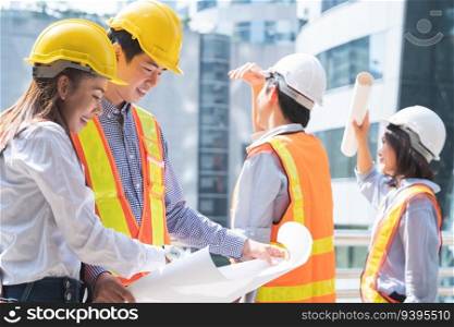 Group of Asian engineers in helmets looking at a blueprint to discuss and plan for build a modern building in city at construction site. Selective focus on engineering woman