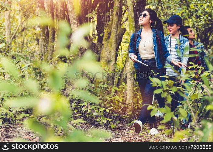 Group of Asian friendship adventure in forest jungle view background. Girl leading tourism team in nature. People lifestyle travel on vacation concept. Summer picnic and camping. Trekking hiking