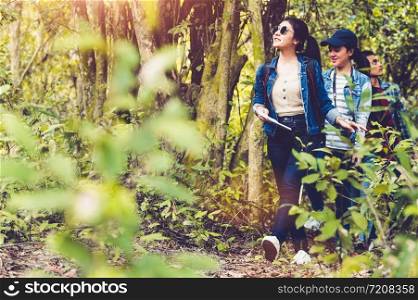 Group of Asian friendship adventure in forest jungle view background. Girl leading tourism team in nature. People lifestyle travel on vacation concept. Summer picnic and camping. Trekking hiking