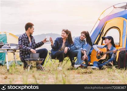 Group of Asian friendship clinking drinking bottle glass for celebrating in private party with mountain and lake view background. People lifestyle travel on vacation concept. Picnic and camping tent