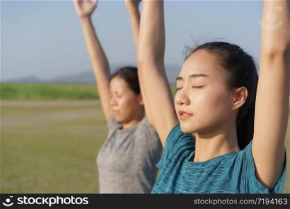 Group of Asian people practicing yoga In the prayer position and raised hands while standing outdoor in the summer, Asia girl take care of their health with meditation. Concept wellness and lifestyle