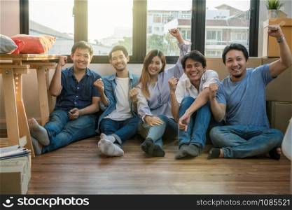 Group of Asian team work are glad after successfull packing the big cardboard box for moving in new house, Moving and House Hunting concept,