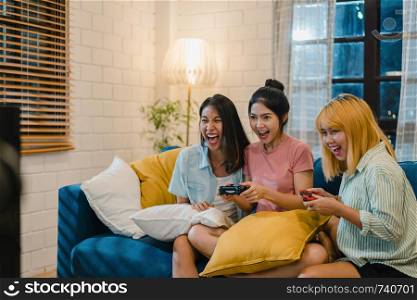 Group of Asian women couple play games at home, female using joystick having funny moment together on sofa in living room in night. Teenager young friend football fan, celebrate holiday concept.