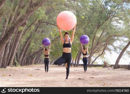 Group of Asian women in yoga class club doing exercise and yoga at natural beach, trees and sand outdoor in sport and recreation concept. People lifestyle activity.