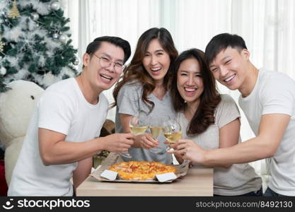 Group of Asian young male and female friends gather to celebrate Christmas, clinking champagne glasses and eating pizza at home. Joy of holiday party with friends or family concept