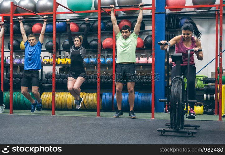 Group of athletes doing pull ups and air bike in the gym. Athletes doing pull ups and air bike in the gym