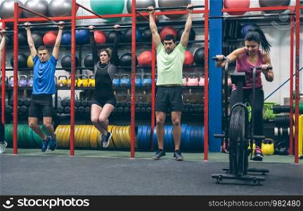 Group of athletes doing pull ups and air bike in the gym. Athletes doing pull ups and air bike in the gym