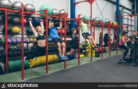 Group of athletes doing pull ups and air bike in the gym. Athletes doing pull ups and air bike in the gym