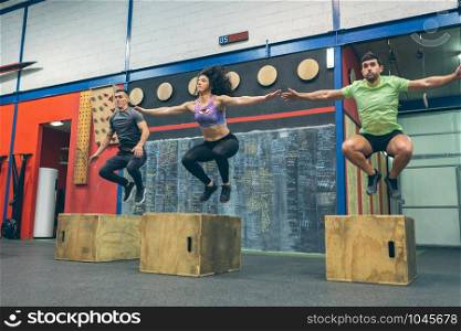 Group of athletes exercising jumping wooden box in the gym. Athletes exercising jumping wooden box