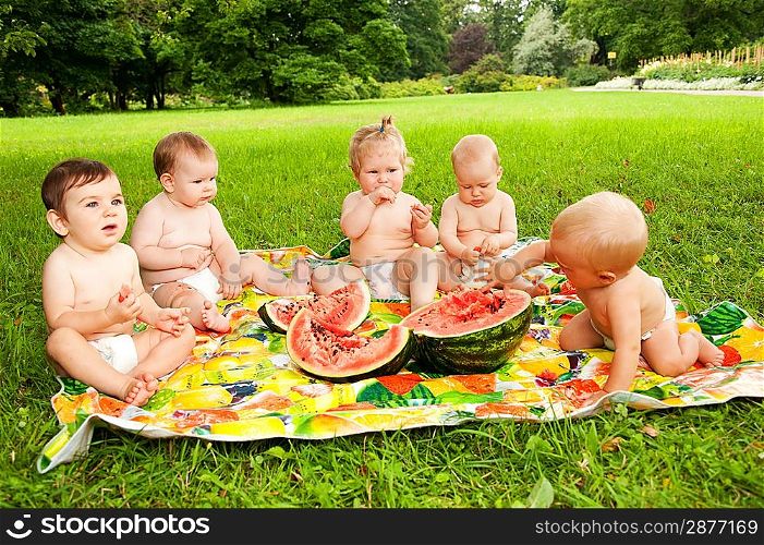 Group of babies eating watermelon outdoors.