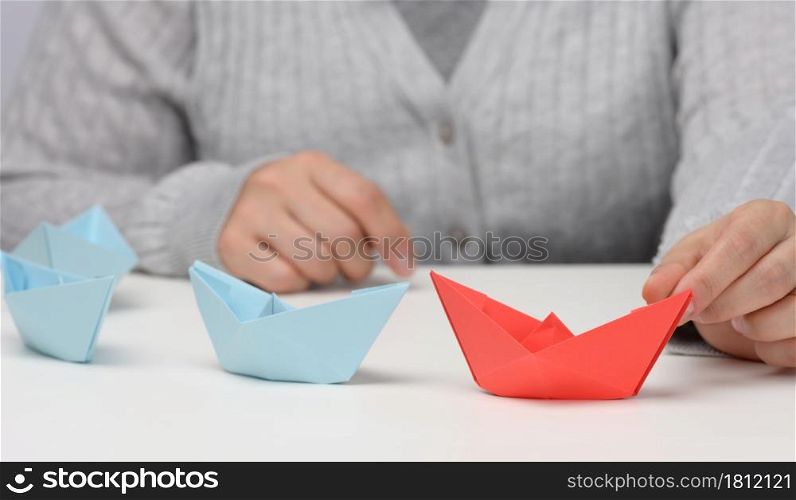 group of blue paper boats follows a red boat in front of a white background. The concept of a strong and charismatic leader in a team, manipulating the masses