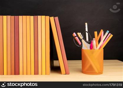 Group of books and pencils on wooden table and blackboard at background. Copy space