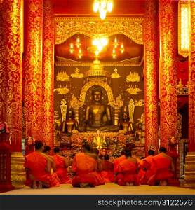 Group of buddhist monks sitting in the temple and praying