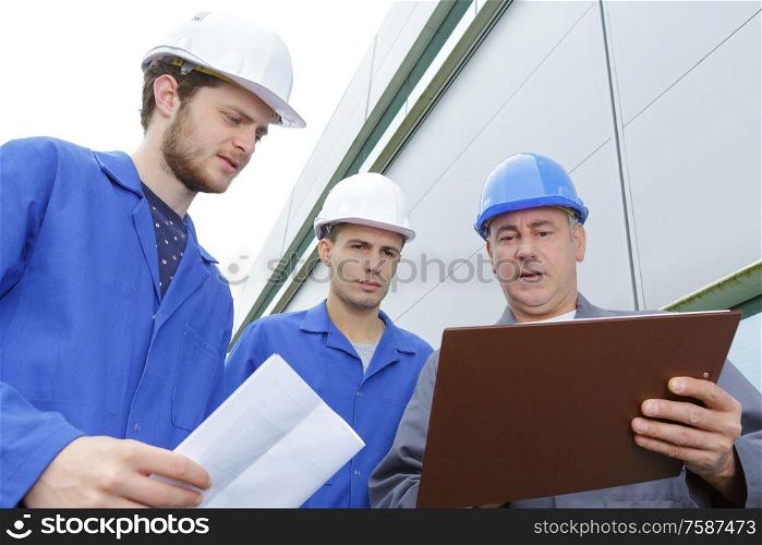 group of builders in hardhats with clipboard outdoors