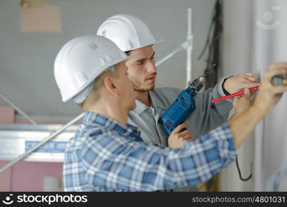 group of builders in hardhats with electric drill indoors