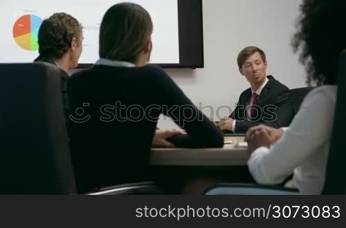 Group of business people meeting in corporate conference room, applauding at a coworker during his presentation. The man is showing charts and slides on a big TV monitor. Medium shot