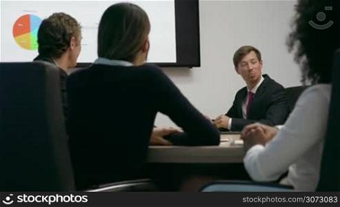 Group of business people meeting in corporate conference room, applauding at a coworker during his presentation. The man is showing charts and slides on a big TV monitor. Medium shot
