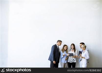 Group of business people standing by the wall and looking at digital tablet in the office