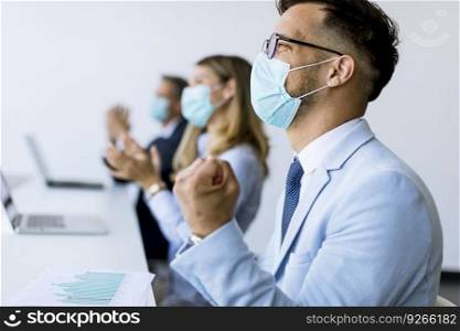 Group of business people with protection masks clapping hands after successful business meeting in the modern office