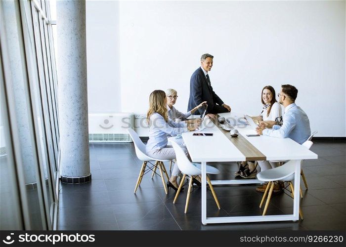 Group of business people with young adults and senior woman colleague on meeting at the modern bright office interior