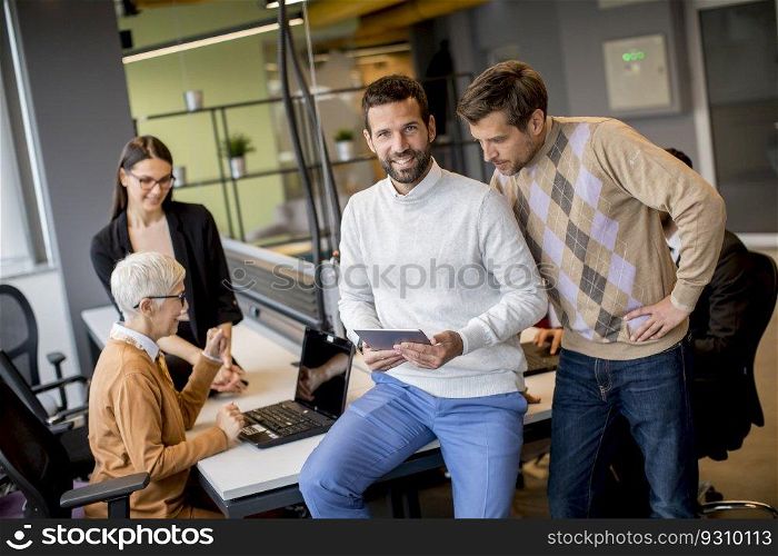 Group of business people working and communicating while standing in  the office together with colleagues sitting in the background