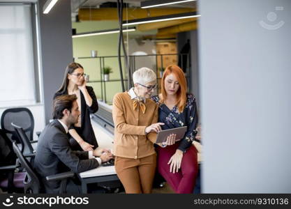 Group of business people working and communicating while standing in  the office together with colleagues sitting in the background