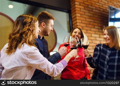 Group of caucasian friends or family standing by the table at winery or restaurant holding a glasses of red wine toasting celebrating young man and three women wearing shirt side back view