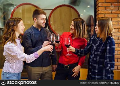 Group of caucasian friends or family standing by the table at winery or restaurant holding a glasses of red wine toasting celebrating young man and three women wearing shirt