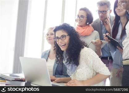 Group of cheerful businesspeople with laptop at desk in creative office