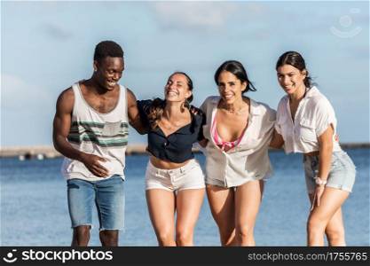Group of cheerful multiracial friends standing in beach and embracing while having fun on Lanzarote in summer. Company of diverse friends hugging at seaside