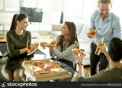 Group of cheerful young people eating pizza in the room and having fun