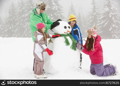 Group Of Children Building Snowman On Ski Holiday In Mountains