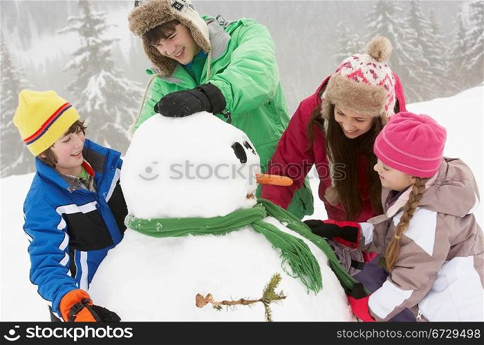Group Of Children Building Snowman On Ski Holiday In Mountains