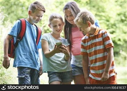 Group Of Children Geocaching Using Mobile Phone In Forest