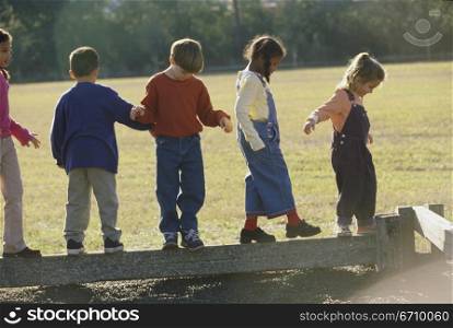 Group of children walking on a wooden log