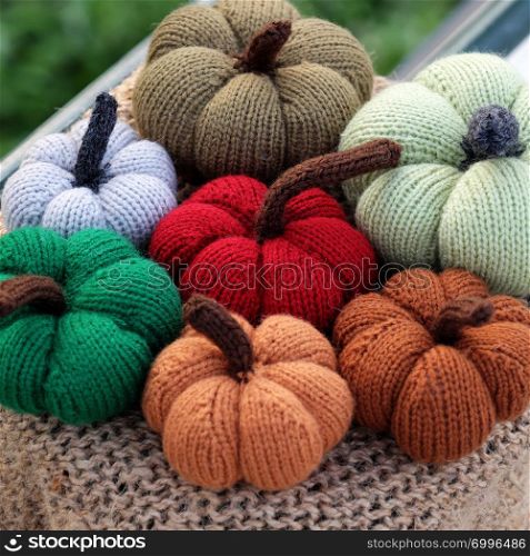 Group of colorful pumpkin ornament knit from yarn on outside table with green background, near banister, photo focus on autumn pumpkins with blurred background