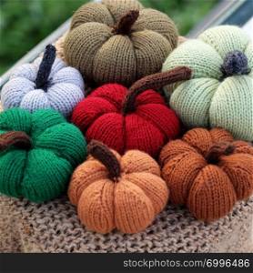 Group of colorful pumpkin ornament knit from yarn on outside table with green background, near banister, photo focus on autumn pumpkins with blurred background