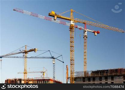 Group of construction cranes on a blue sky background.
