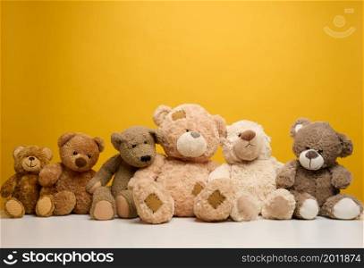 group of cute brown teddy bears sit on yellow background, childrens toy