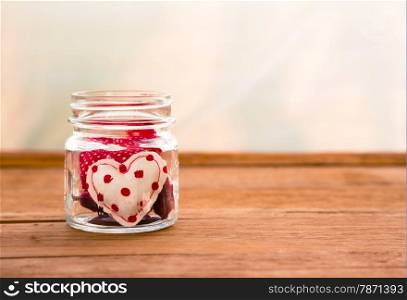 Group of cute red tone hearts handmade crafts from cotton and silk cloth in glass jar place on wood surface with white curtain on background, love and valentine&rsquo;s day symbol