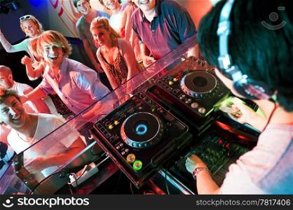 Group of dancing people in front of a dj in a discotheque