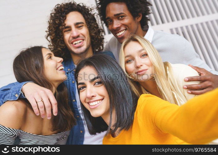 Group of delighted diverse friends embracing and taking self shot while having fun and looking at camera. Company of multiethnic friends taking selfie