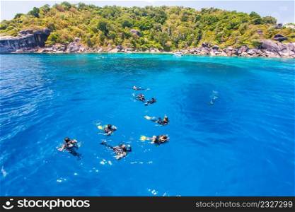 Group of divers in diving suit staying afloat in the sea for a dive. Colorful tropical sea in summer, turquoise seawater with green island background. Similan Islands, Andaman sea, Thailand.