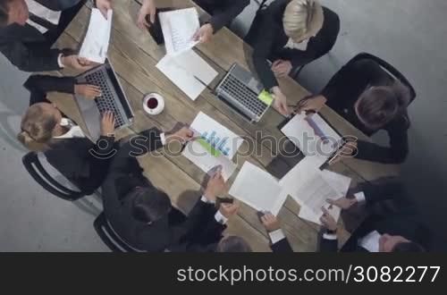 Group of diverse business executives holding a meeting around a table discussing graphs charts showing statistical data analysis