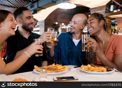 Group of diverse friends clinking their beer glasses while enjoying a meal together at a restaurant. Friends concept.